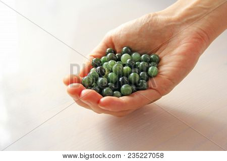 Natural Green Jade Nephrite Mineral Stones Beads. The Green Jade Stone Lies In The Hands. Hands Hold