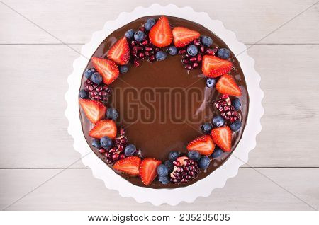 Birthday Cake In Chocolate With Strawberries, Blueberries And Garnet On White Wooden Table. Top View