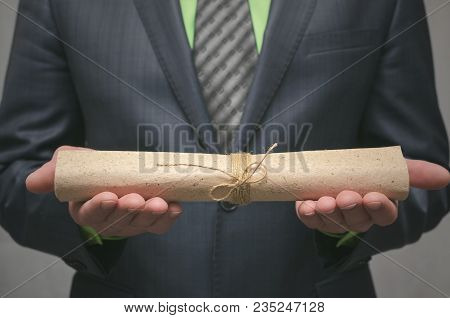 Businessman Holds In Hand A Rolled Up Document Scroll. Signing Of An Agreement. Conclusion Of A Busi