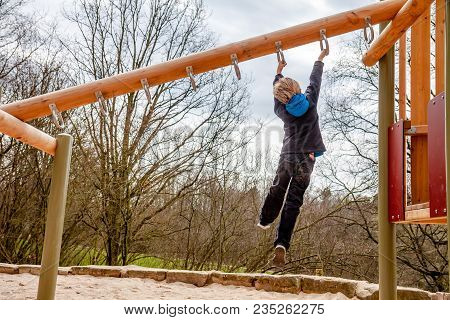 Happy Boy Hanging On Ladder In The Playground Outdoors