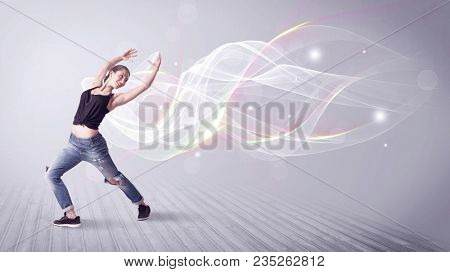 A beautiful young hip hop dancer dancing contemporary urban street dance in front of grey wall background with smokey lines and glitter concept.
