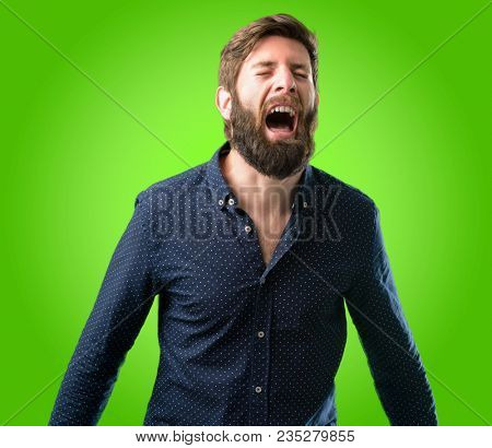 Young hipster man with big beard stressful, terrified in panic, shouting exasperated and frustrated. Unpleasant gesture. Annoying work drives me crazy over green background