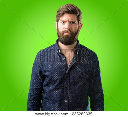 Young hipster man with big beard making funny face fooling over green background