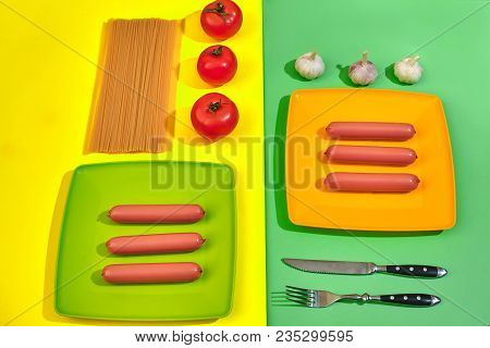 A Lot Of Raw Sausages On Plate. On Green And Yellow Background With Pasta And Vegetables, Top View. 