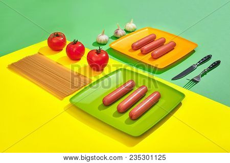 A Lot Of Raw Sausages On Plate. On Green And Yellow Background With Pasta And Vegetables, Top View. 