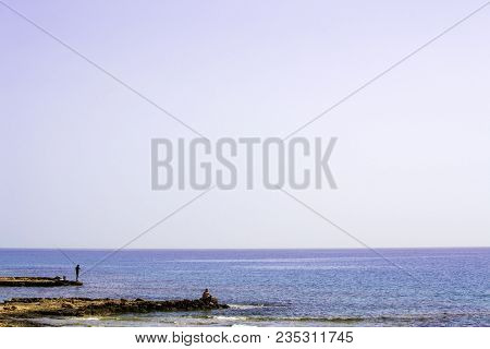 Two Fishermans Staying On The Rocky Shore With Rods