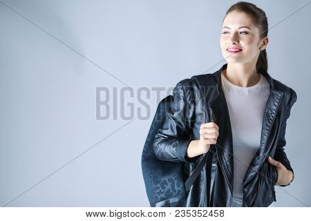 portrait of beautiful young brunette woman in stylish black jacket on gray.