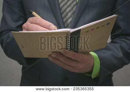 Businessman Is Writing Text In Note Pad In His Hands By The Pen. To Do List. Goals Or Business Trick