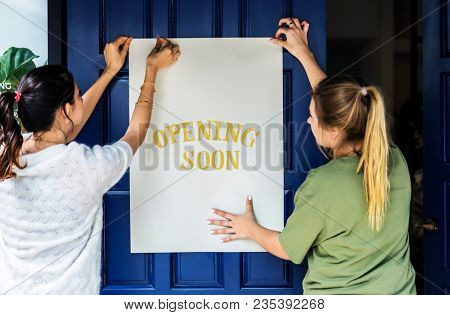 Women putting on store opening soon sign