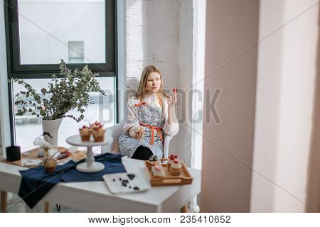 Beautiful Young Woman With Pensive Expression Having Cupcake, Looking At Window, Sitting At The Tabl