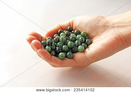 Natural Green Jade Nephrite Mineral Stones Beads. The Green Jade Stone Lies In The Hands. Hands Hold