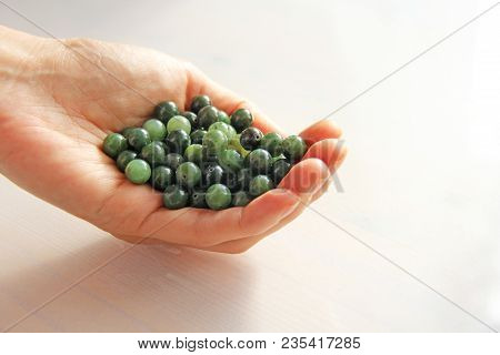 Natural Green Jade Nephrite Mineral Stones Beads. The Green Jade Stone Lies In The Hands. Hands Hold