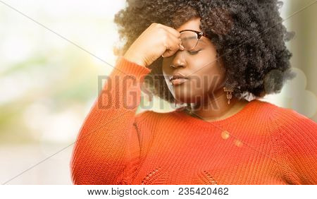 Beautiful african woman with sleepy expression, being overworked and tired, rubbes nose because of weariness, outdoor