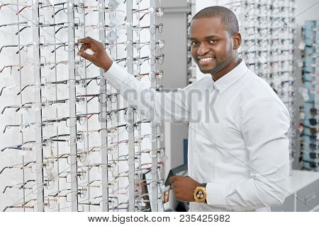 Sideview Of Smiling Man Is Choosing Eyeglasses In Optical Shop. Model Is Wearing Snowwhite Classic S
