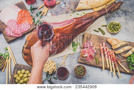 Mans Hand Holding Wine Glass Frome Above Table With Spanit Or Italian Appetizers, Whole Leg Of Ham S