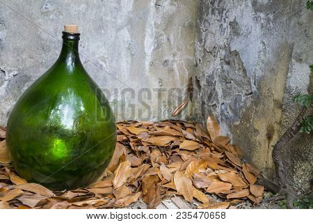Closeup Of Green Glass Carboy On Dry Leaves