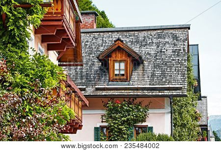 Hallstatt Austria. Houses with wooden balconies, windows and roofs. Racy antique traditional austrian houses among greenery, bushes and flowers.