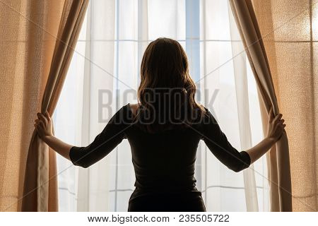 Young Woman Opens The Curtains At The Panoramic Window