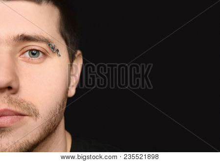 Young man with pierced eyebrow on black background