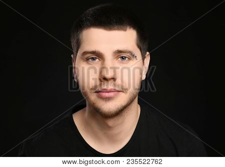 Young man with pierced eyebrow on black background