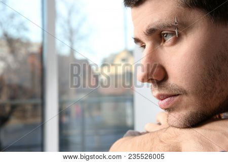 Young man with pierced eyebrow near window