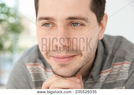 Portrait of young man with pierced eyebrow on blurred background, closeup