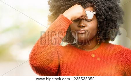 Beautiful african woman with sleepy expression, being overworked and tired, rubbes nose because of weariness, outdoor