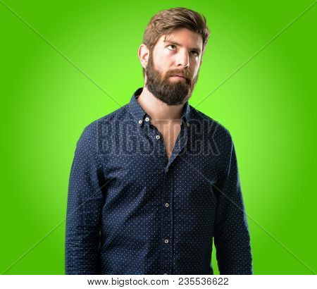 Young hipster man with big beard making funny face fooling over green background