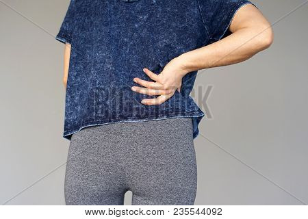 Close-up View Of A Young Woman With Pain In Kidneys Isolated On Gray Background. Young Woman With Ba