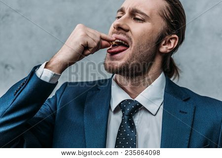 Close-up Portrait Of Addicted Businessman Taking Mdma Pill In Front Of Concrete Wall