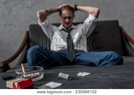 Depressed Businessman With Drug Addiction Sitting On Couch In Front Of Table With Mdma Pills