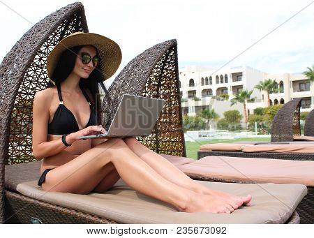 Work And Travel. Incredibly Sexy Girl In A Black Bikini Sits With A Laptop Near The Pool. Find A Tou