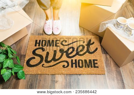 Wman in Pink Shoes and Sweats Standing Near Home Sweet Home Welcome Mat, Boxes and Plant.