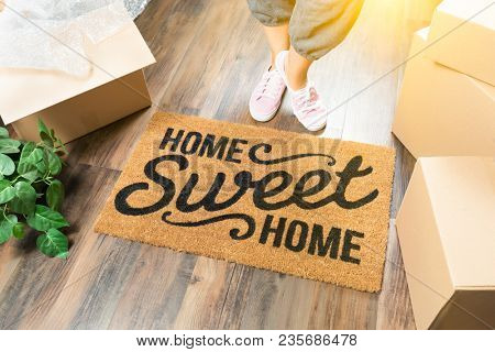 Wman in Pink Shoes and Sweats Standing Near Home Sweet Home Welcome Mat, Boxes and Plant.