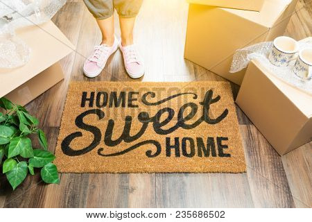 Wman in Pink Shoes and Sweats Standing Near Home Sweet Home Welcome Mat, Boxes and Plant.