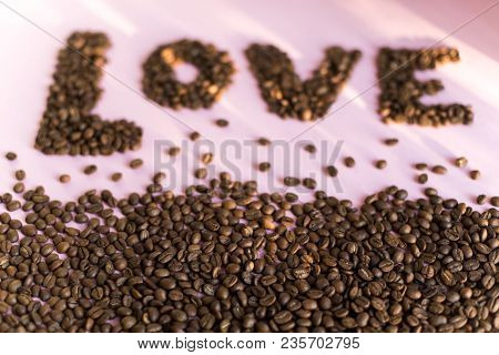 Spilled Roasted Coffee Beans On A Pink Background With A Love Inscription.