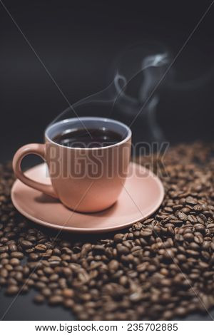 Cup Of Black Steaming Coffee On A Spilled Roasted Coffee Beans On A Black Background.