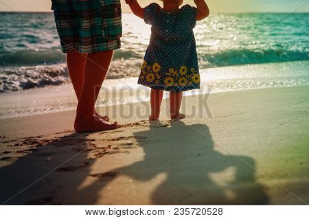 Silhouette Of Father And Little Daughter Walk At Sunset Beach