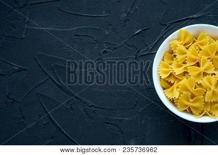 Farfalle Raw Pasta In A White Bowl On A Black Textured Background From The Side. Close-up With The T