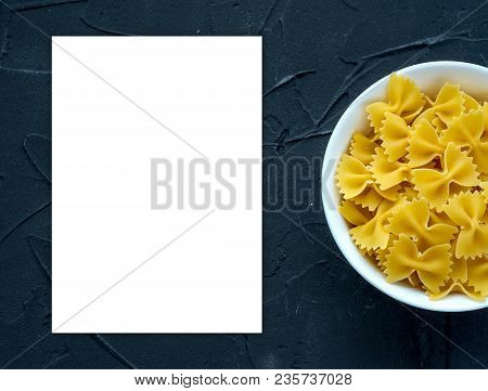 Farfalle Raw Pasta In A White Bowl On A Black Textured Background From The Side. Close-up With The T