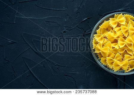 Farfalle Raw Pasta In A Glass Cup On A Black Textured Background From The Side. Close-up With The To