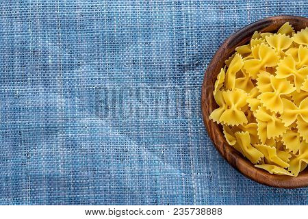 Farfalle Raw Pasta In Wooden Bowl On Blue Knitted Textured Background With Side. Close-up With The T
