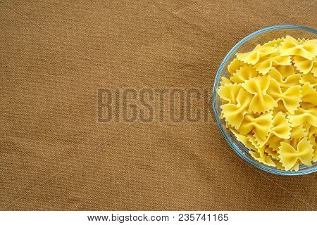 Farfalle Raw Pasta In A Glass Cup On A Brown Suburban Background Texture With A Side. Close-up With 
