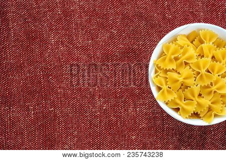 Farfalle Raw Pasta In A White Cup On A Red Brown Rustic Texture Background, In The Center Close-up F