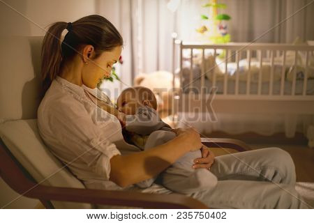Young Beautiful Mother, Breastfeeding Her Newborn Baby Boy At Night, Dim Light