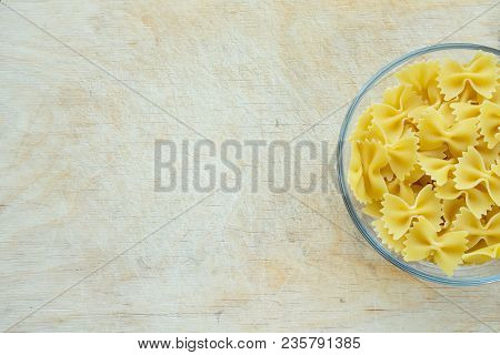 Farfalle Raw Farfallini Pasta In A Glass Cup On A Wooden Table Textured Background With A Side. Clos