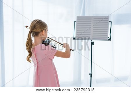 Back View Of Little Child In Pink Dress Playing Violin At Home
