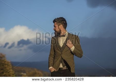 Hipster With Stylish Appearance In Front Of Dramatic Sky. Man With Beard And Mustache With Scenery O