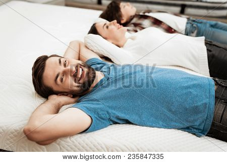 Young Happy Couple With Cute Little Boy Lies On Bed In Mattress Store. Family Checking Softness Of M
