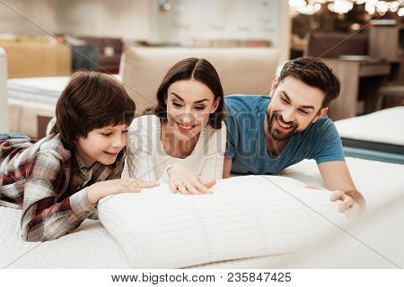 Young Beautiful Woman And Bearded Man With Cute Little Boy Lies On Bed In Mattress Store. Family Che